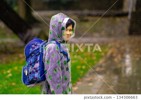 A child in a raincoat with a school bag goes to school in the rain. 134306663