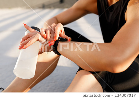 Close-up of female hands holding a sports bottle and checking smartwatches during a workout Close-up of female hands holding a sports bottle and checking smartwatches during a workout 134307017