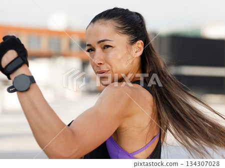 Woman doing high-intense warming up. High detailed portrait of a muscular athlete practicing punches outdoors. Woman doing high-intense warming up. High detailed portrait of a muscular athlete practicing punches outdoors. 134307028