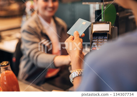 View from the shoulder of the customer paying by card at pos terminal in a grocery store View from the shoulder of the customer paying by card at pos terminal in a grocery store 134307734