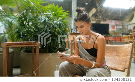 A casual woman is engaging with her smartphone amidst the lush urban greenery of her environment A casual woman is engaging with her smartphone amidst the lush urban greenery of her environment 134308121