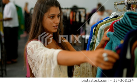A young woman shops for trendy clothes at a boutique filled with stylish attire and accessories A young woman shops for trendy clothes at a boutique filled with stylish attire and accessories 134308124