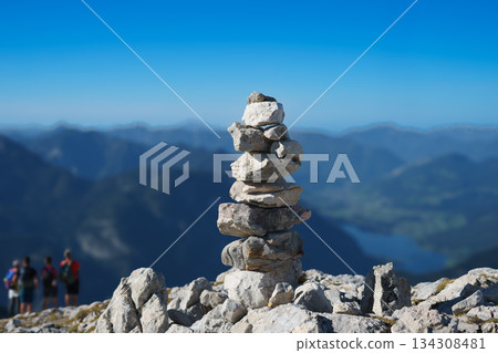 Stone pyramid in the mountains on the top, laid out on a hiking trail against the backdrop of the Alps and blue sky Stone pyramid in the mountains on the top, laid out on a hiking trail against the backdrop of the Alps and blue sky 134308481
