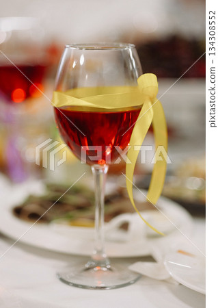Red wine glass with yellow ribbon on festive table 134308552