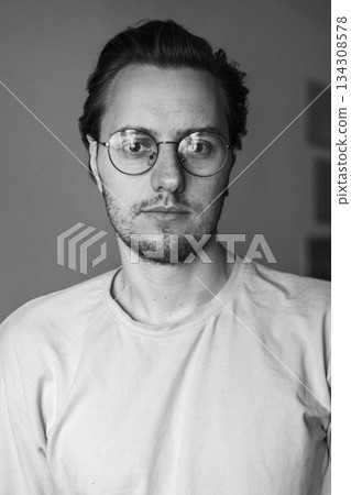 Black and white portrait of young man wearing glasses indoors Black and white portrait of young man wearing glasses indoors 134308578