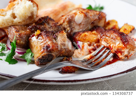 A plate with the remains of a pork kebab, there are no people. 134308737