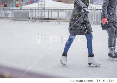 People ice skating outdoors during snowfall, dressed in warm winter clothes. Concept of winter activity, cold season lifestyle, active outdoor fun. Winter background, copy space People ice skating outdoors during snowfall, dressed in warm winter clothes. Concept of winter activity, cold season lifestyle, active outdoor fun. Winter background, copy space 134309152