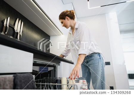 Woman loading dishwasher in modern home kitchen. Woman loading dishwasher in modern home kitchen. 134309268