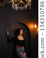 Caucasian woman posing by dark textured wall with warm lightbulb in moody room 134310786