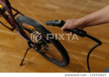 High-angle view of man cleaning bicycle tire with steam cleaner, removing dirt and grime for precise maintenance of cycling equipment at home, close-up. Concept of bike maintenance and service. 134310825