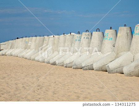 A row of concrete tetrapods stands on a sandy beach by the sea. A row of concrete tetrapods stands on a sandy beach by the sea. 134311275