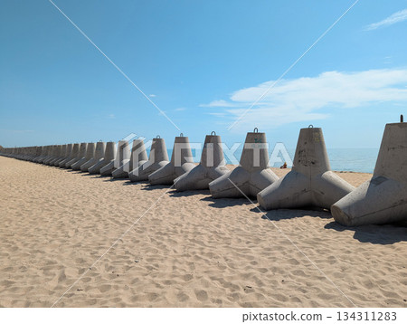 Heavy concrete tetrapods lie on a bright sandy shore. 134311283