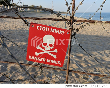 Chernomorsk, Ukraine, July 27, 2025: Warning mine sign placed on a quiet sandy beach. Chernomorsk, Ukraine, July 27, 2025: Warning mine sign placed on a quiet sandy beach. 134311288