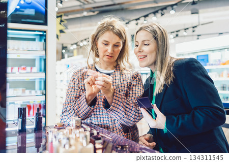 Two cheerful friends are choosing mascara and lipstick in cosmetics store 134311545