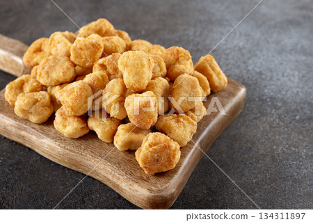 Crispy chicken popcorn on a wooden serving board against a gray background. Close-up. Fast food and snack concept. 134311897