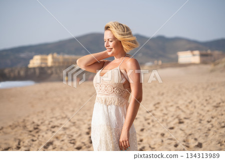 Cheerful blond woman standing on sandy beach 134313989