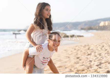 Happy girls playing piggyback ride on sandy beach 134313990