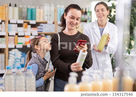 Middle-aged woman with daughter scanning barcode on shampoo in drugstore Middle-aged woman with daughter scanning barcode on shampoo in drugstore 134317540