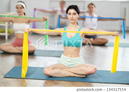 Young girls doing arm workout with band sitting cross-legged Young girls doing arm workout with band sitting cross-legged 134317554