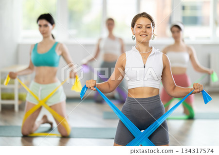 Young girl doing arm workout with resistance band standing on knees 134317574