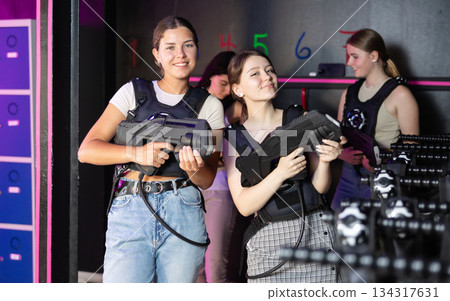 Portrait of two positive girls in special vests playing laser tag with friends on bachelorette 134317631