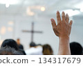 A believer raising a hand in prayer and worship during a church service. The soft focus and added film grain create a classic, emotional atmosphere. Ideal for themes of faith, worship, devotion, and s 134317679
