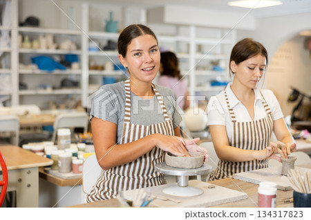Two young women pottery workshop workers sculpt from raw clay Two young women pottery workshop workers sculpt from raw clay 134317823