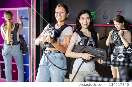 Two cheerful and happy girls friends pose in locker room before laser tag match. Two cheerful and happy girls friends pose in locker room before laser tag match. 134317840