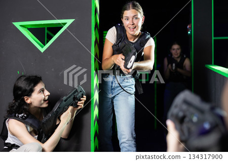 Team of young girlfriends play laser tag in labyrinth. Girls spend time actively Team of young girlfriends play laser tag in labyrinth. Girls spend time actively 134317900