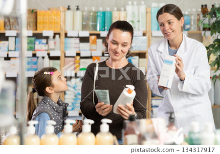 Middle-aged woman with daughter choosing cream in drugstore 134317917