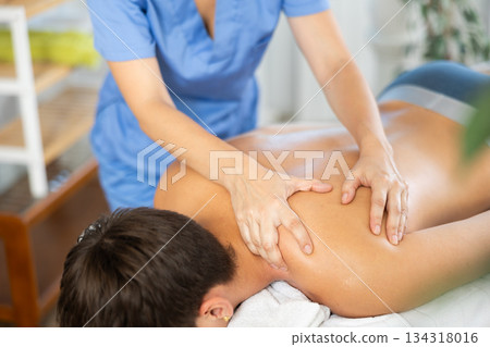 Close up of woman hands of massager woman doing massage to young man in spa salon Close up of woman hands of massager woman doing massage to young man in spa salon 134318016