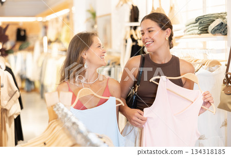 Two young women choosing a dress and other clothes in clothing store 134318185