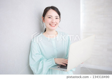 A woman looking at the camera while operating a computer by the wall 134318490
