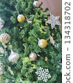 Decorated Christmas tree with ornaments and decorations. The ornaments include golden spheres, silver bulb-shaped objects, snowflake-shaped objects, and a star-shaped ornament 134318702