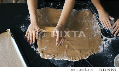 Hands roll ginger cookie dough on a floured surface as a mother and daughters work together in a warm kitchen 134319495