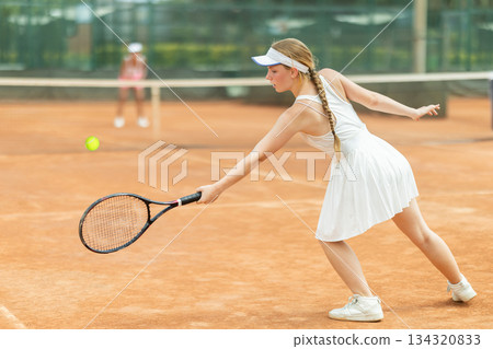 Woman playing tennis against female opponent on tennis court 134320833