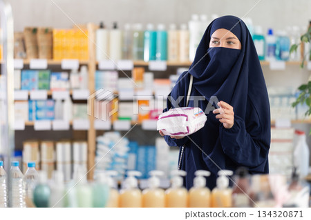 Young woman in hijab chooses feminine pads at pharmacy 134320871