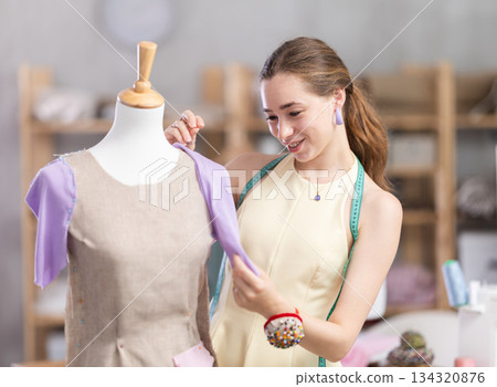 Female tailor sews new dress on a mannequin in sewing studio Female tailor sews new dress on a mannequin in sewing studio 134320876