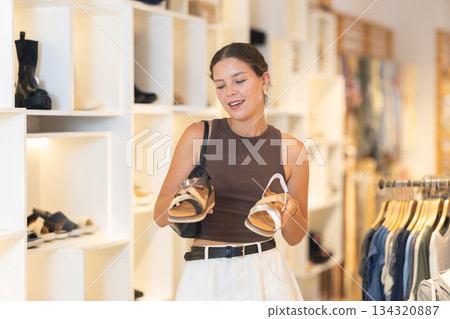 Young woman standing in a clothing store and choosing shoes 134320887