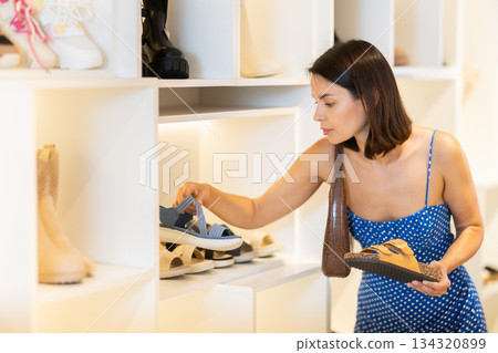 Young woman standing in a clothing store and choosing shoes Young woman standing in a clothing store and choosing shoes 134320899