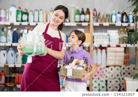 Friendly female salesperson helping little girl choose gift in goods store Friendly female salesperson helping little girl choose gift in goods store 134321007