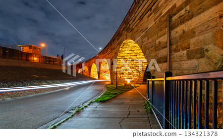 Stone Arch Bridge features illuminated arches at night in Minneapolis. Long exposure captures light trails on West River Parkway under a cloudy sky 134321378