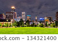 Night view of downtown Minneapolis skyline from The Commons park. Illuminated skyscrapers and historic Armory rise beyond the green lawn under a cloudy sky 134321400