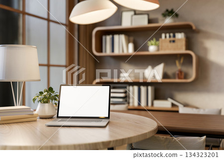 Blank screen laptop on round wooden table under lamp light and bookshelf in a living room or library 134323201
