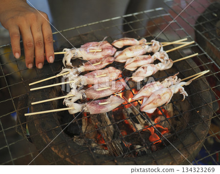 Grilled squid street food seafood skewers charcoal barbecue market hand touch warmth with savory aroma and joy 134323269