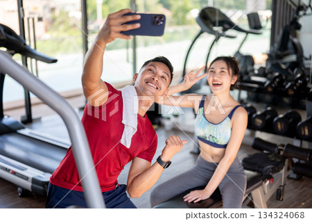 Fitness trainer coach holding phone taking picture photo with woman client after exercising in a gym 134324068