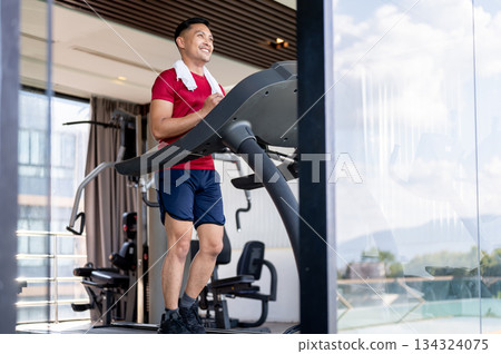 Asian middle aged strong healthy man with a towel on shoulder running exercising on treadmill in gym Asian middle aged strong healthy man with a towel on shoulder running exercising on treadmill in gym 134324075