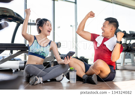 Asian woman client and fitness coach trainer a raising fist sitting on floor after exercising in gym Asian woman client and fitness coach trainer a raising fist sitting on floor after exercising in gym 134324082