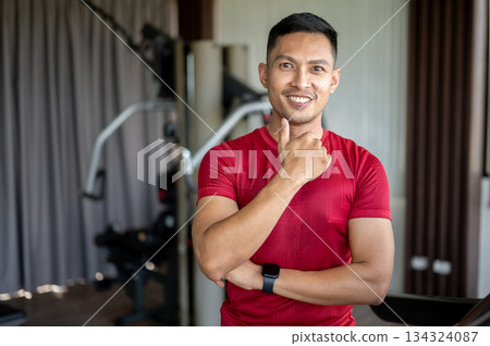 Asian middle aged healthy man fitness trainer standing and making a thumb up after exercising in gym Asian middle aged healthy man fitness trainer standing and making a thumb up after exercising in gym 134324087