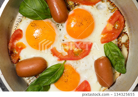 Fried eggs in the pan. Fried eggs with sausages and vegetables. Fried eggs in the pan. Fried eggs with sausages and vegetables. 134325655